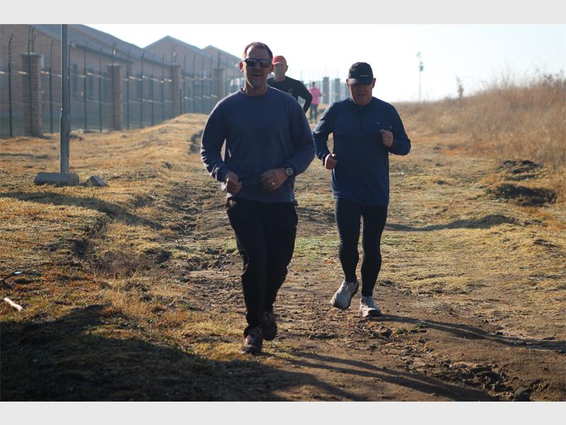 Two men running on a dirt road near a fence.