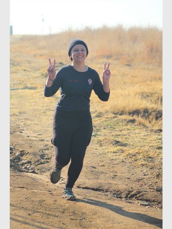 A woman running on a dirt road with her hands up.