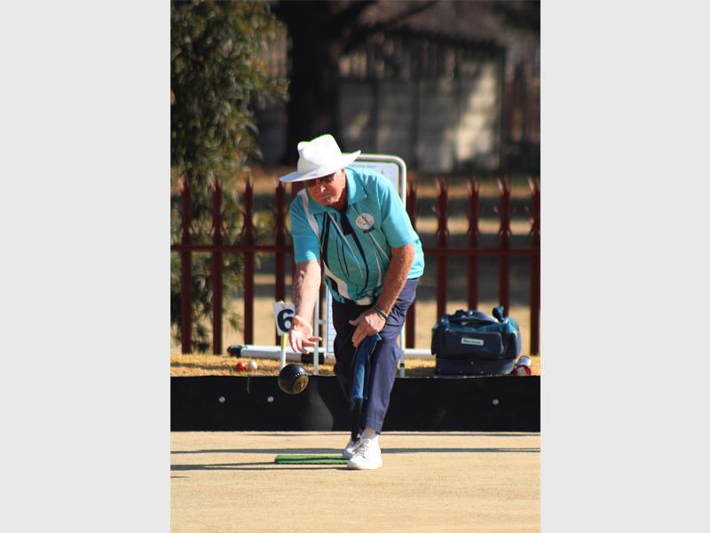 A man in a hat playing lawn bowls.