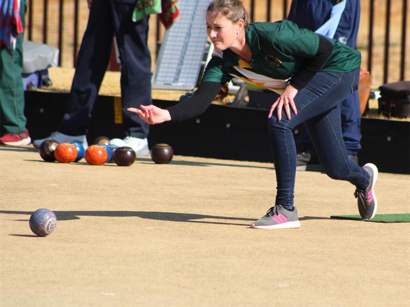 A woman in green shirt and black pants is about to throw a bowling ball.