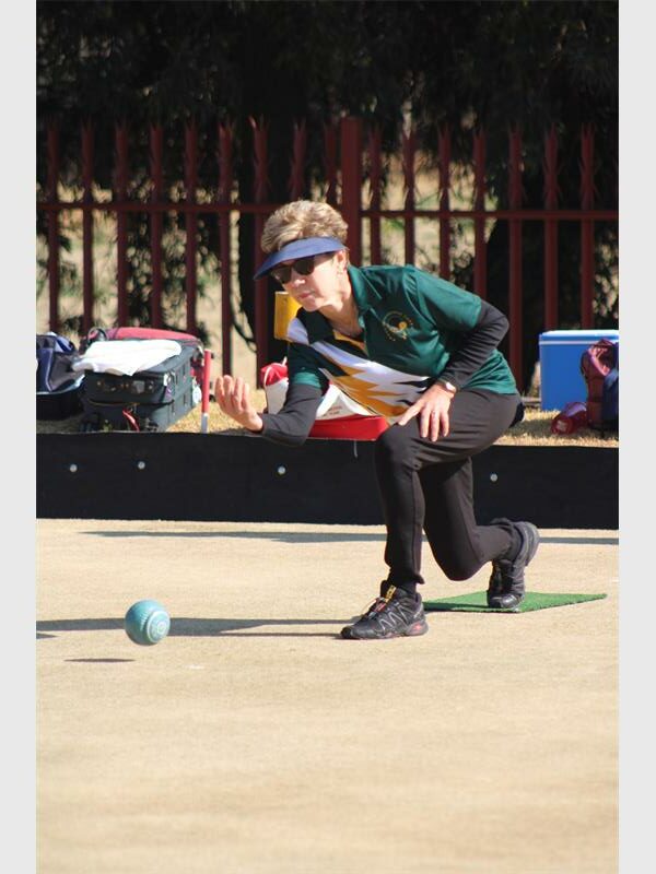 A young boy in a green shirt and black pants is playing a game of bowls.