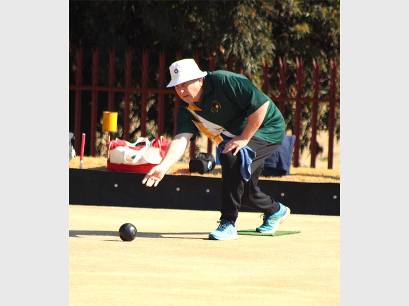 A man in a green shirt and hat playing a game of bowls.