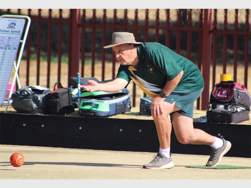 A man in a hat and green shirt playing a game of bowls.