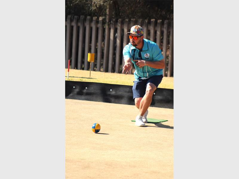 A man in a blue shirt and sunglasses playing a game of bocce.