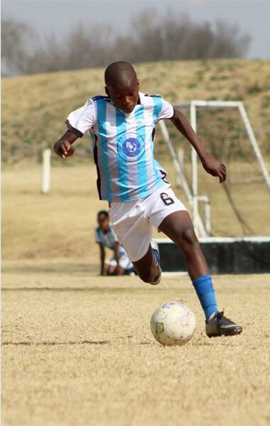 A young boy in a blue and white uniform is kicking a soccer ball.