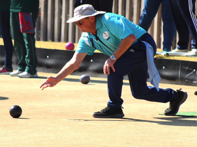 A man in a blue shirt and hat is playing a game of bowling.