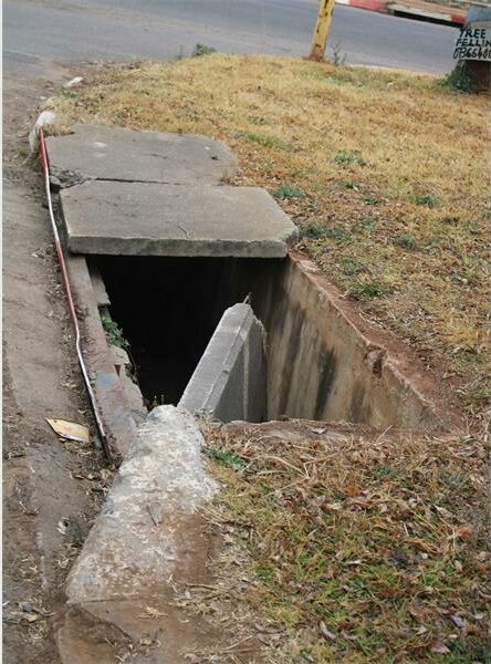 A man is standing in the open hole of a sewer.