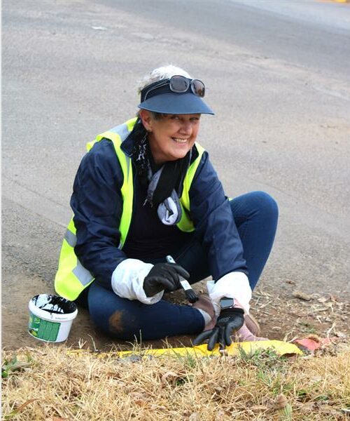 A woman in a safety vest and gloves sitting on the ground.