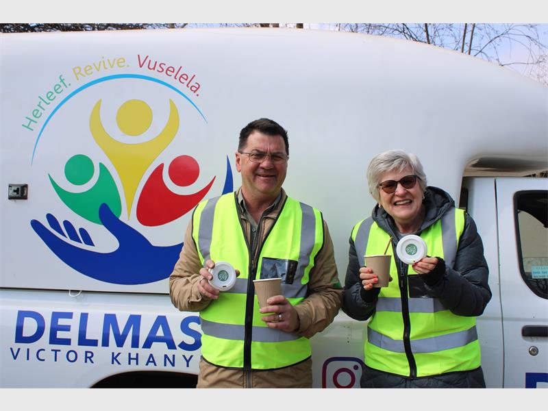 Two men in vests holding a sign that says delmas.