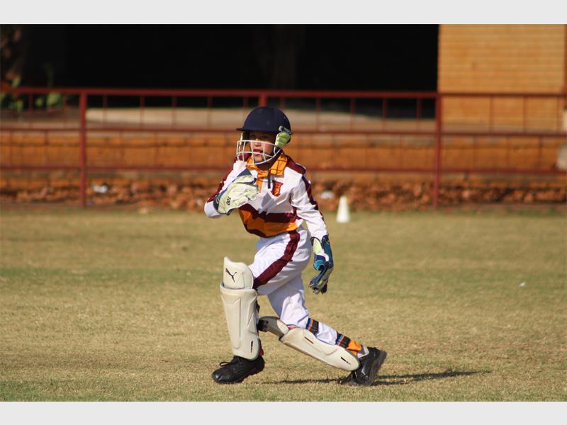 A young boy in a white and maroon uniform is playing cricket.