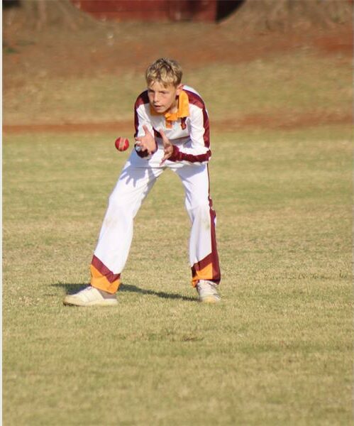 A boy in a white and maroon uniform playing cricket.
