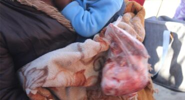 A woman holding a baby and a piece of meat.