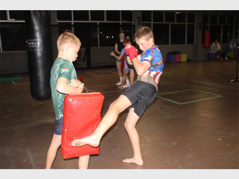 Two boys are kicking a red pad in an indoor gym.