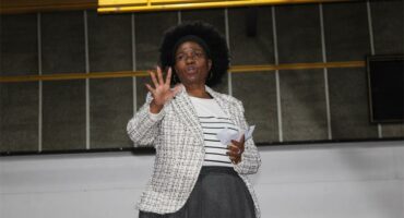 A woman in a suit and blazer giving a speech.