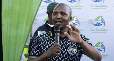 A man in a black shirt and green shirt speaking into a microphone.