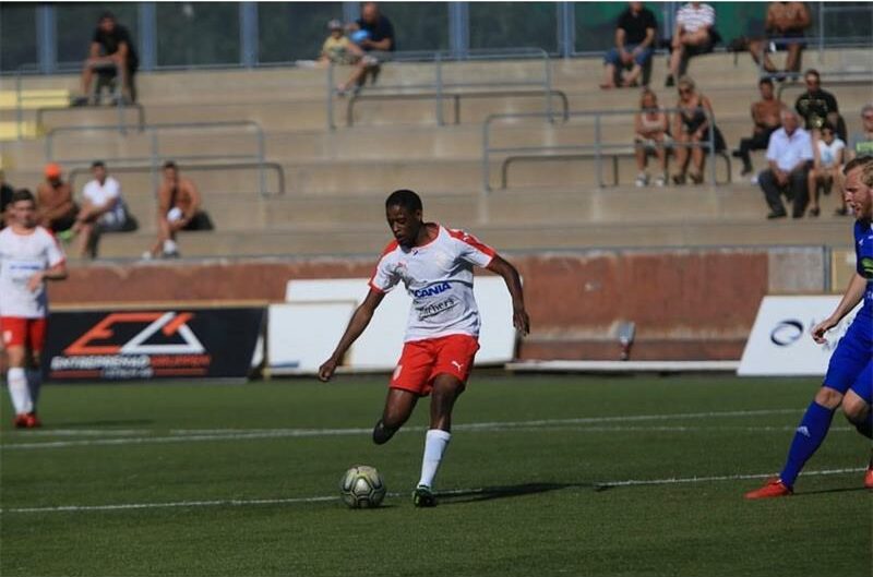 Young soccer player kicking ball during match at Ridge Times event, with spectators in stands.