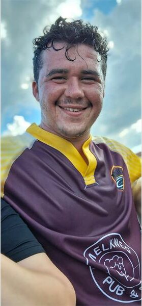A man in a maroon and gold jersey is smiling.