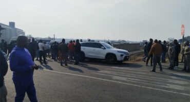 People standing around a white suv on the side of the road.