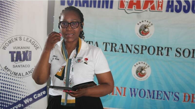 A woman in glasses holding a microphone and talking.