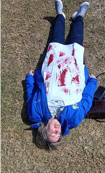 A woman laying on the ground with blood on her clothes.
