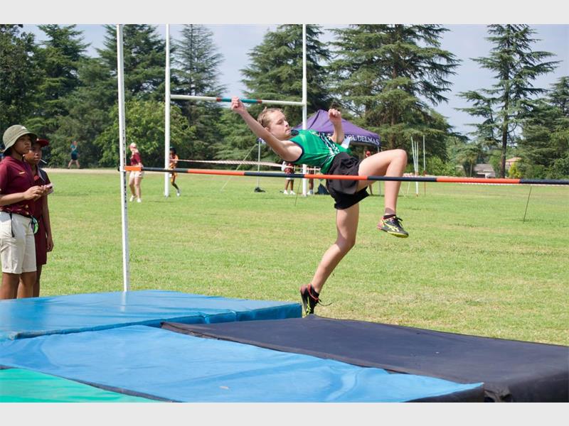 A girl in green shirt and black shorts jumping over a high jump.