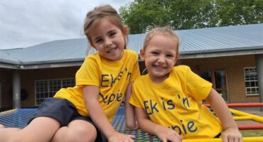 Two young girls wearing yellow shirts sitting on a blue playground.