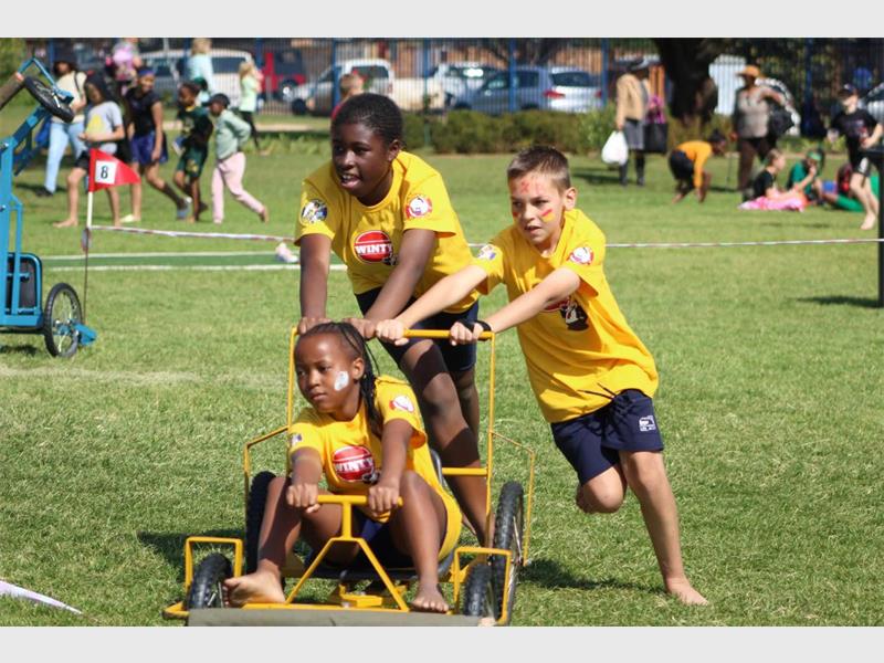 Three children in yellow shirts are pulling a cart.