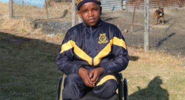 A young boy in a wheelchair sitting on a grassy field.