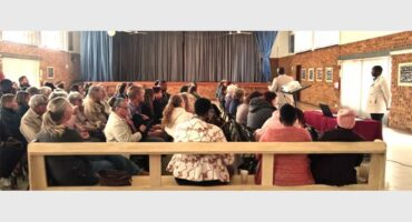 A group of people sitting in a room with a man standing.