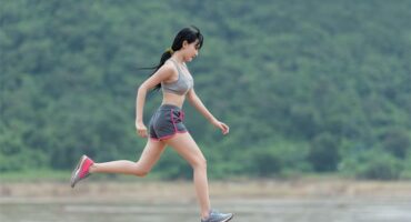 A woman running on a dirt road near a river.