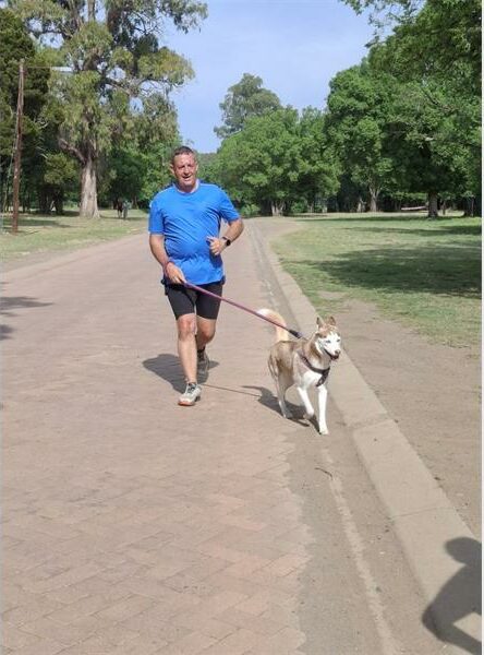 Man in a blue shirt runs with his dog on leash.