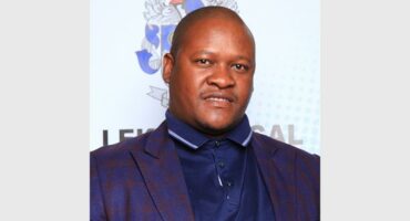 head and shoulder image of a man in front of a code of arms