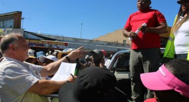 Man with paper in his hand speaks to another standing atop a bakkie