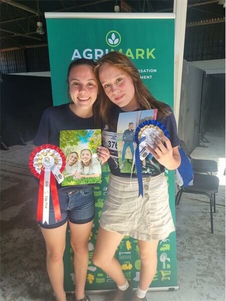 Twee meisies met rosette voor 'n groen advertensiebord