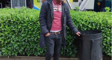 A man stand s in front of a hedge.