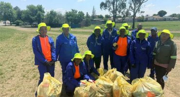 A group of workers in yellow hats pose with bags of trash.