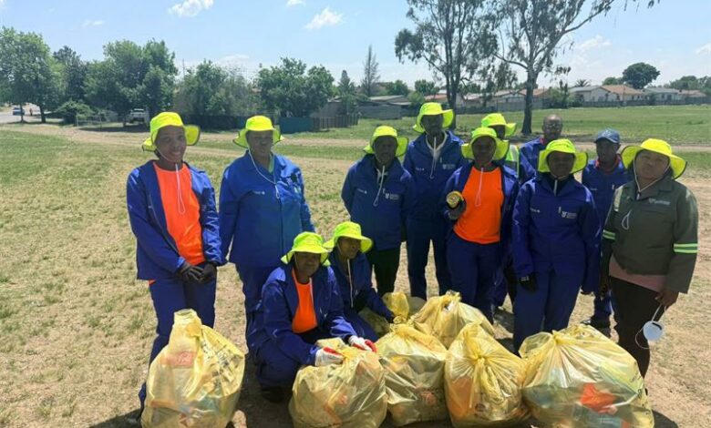 A group of workers in yellow hats pose with bags of trash.
