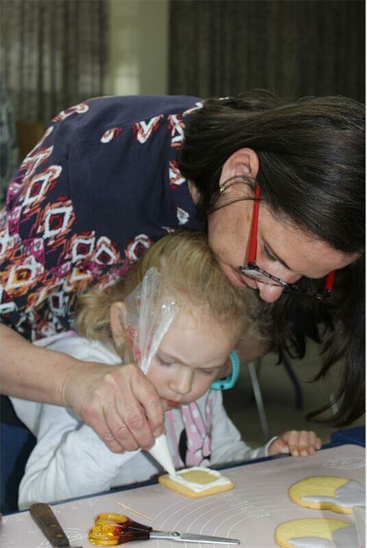 woman helps girl decorate a biscuit.