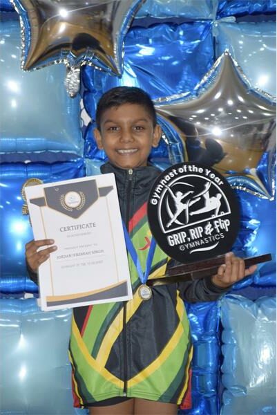 boy in tracksuit holds up certificate and a trophy