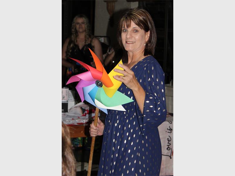 woman in blue dotted dress holds up a colourful fan