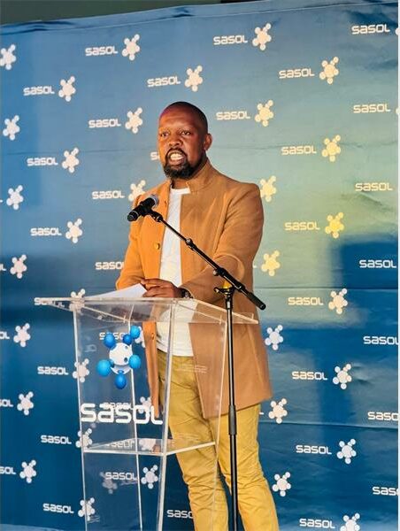 man in brown suit stand behind a podium stand