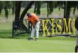 Golf player in orange shirt putts in front of a foot bridge