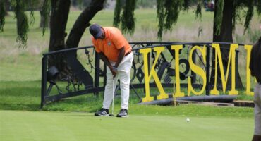 Golf player in orange shirt putts in front of a foot bridge