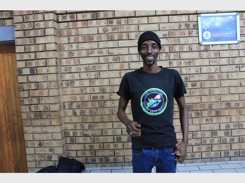 man in black t shirt stands in front of a brick wall