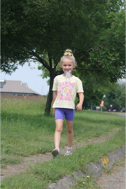 little girl with water sachet in mouth walks on the grassy pavement