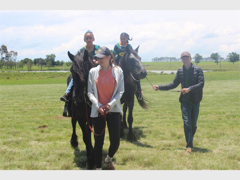 two people lead kids on horses