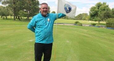 man with turquois shirt on golf course and a flag