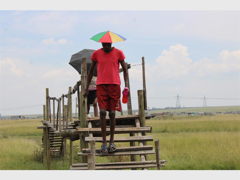 Man walking on wooden bridge with colourful umbrella in open field