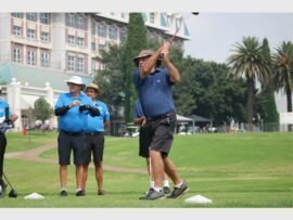 man in dark shirt tees off while two others in sky blue shirts looks on