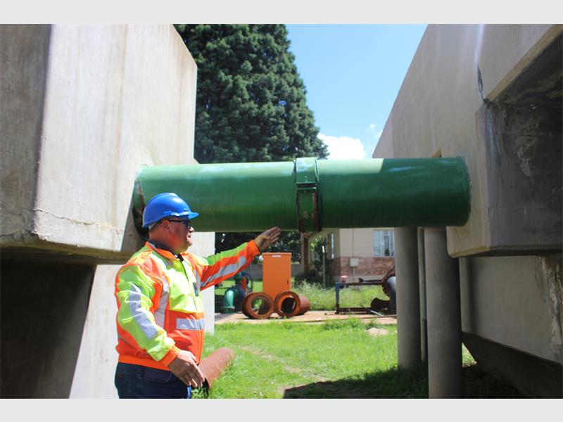 man with hard hat points to leaking pipe